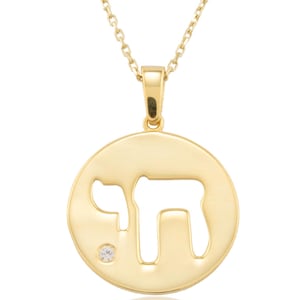 May include: A gold pendant necklace. The pendant is a circular charm with the Hebrew word "Chai" cut out. A small, clear gemstone is set into the charm. The necklace has a delicate chain.