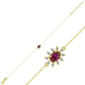 May include: A gold bracelet with a red gemstone surrounded by smaller white gemstones. The bracelet has a delicate chain design.