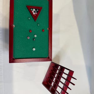 May include: Miniature pool table with a green felt surface and red wooden frame. The table includes a rack of small, colorful balls and a separate red wooden ball return. A fun, decorative item.