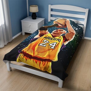 Puede incluir: Un juego de sábanas de cama doble de baloncesto negro y amarillo con un gráfico de un jugador de baloncesto en el aire, vistiendo una camiseta amarilla con el número 24 y la palabra "LAKERS" en ella. El fondo es azul oscuro con estrellas blancas.