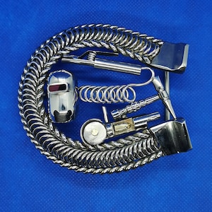 May include: A silver chain bracelet with a silver welder's helmet charm, a silver spring, and a silver tool charm. The bracelet is on a blue background.