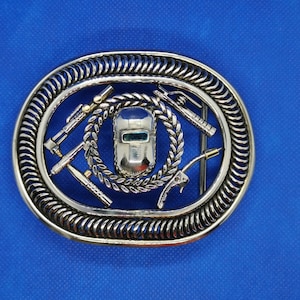 May include: Silver belt buckle featuring an intricate design of a welding mask, welding torch, and a chain. The buckle is oval shaped and has a textured border.