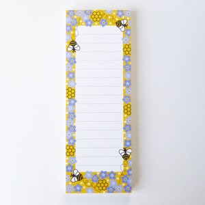 May include: A yellow notepad with a border of blue flowers, honeycombs, and bees. The notepad has lined paper for writing.