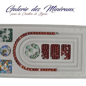Peut inclure: Un plateau de fabrication de bijoux gris avec une rainure circulaire pour enfiler des perles. Le plateau comporte plusieurs compartiments pour ranger les perles. Les compartiments contiennent des perles rouges, vertes et multicolores. Le plateau comporte également une règle le long du bord.