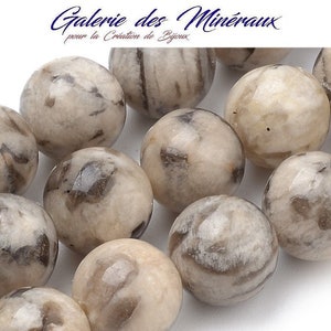 Peut inclure: Gros plan sur un brin de perles rondes en pierre précieuse blanche et grise. Les perles ont un aspect marbré et moucheté.