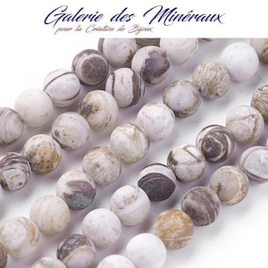 Peut inclure: Gros plan sur une collection de perles rondes en pierre naturelle. Les perles sont principalement blanches avec des veines et des motifs bruns et gris. L'image comprend le texte "Galerie des Minéraux pour la Création de Bijoux" en haut à gauche.