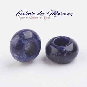 Puede incluir: Dos cuentas redondas de color azul oscuro con un agujero en el centro. Las cuentas están hechas de una piedra moteada.