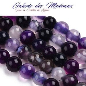 May include: A strand of purple and white agate beads. The beads are round and have a smooth, polished finish. The beads are strung on a clear elastic cord.