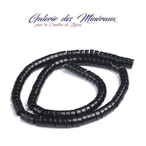 Puede incluir: Un hilo de cuentas negras brillantes en forma de disco dispuestas en una espiral suelta. Sobre las cuentas, el texto dice Galerie des Minéraux pour la Création de Bijoux en una fuente azul oscuro sobre un fondo blanco.
