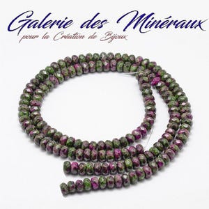 Puede incluir: Un hilo de cuentas redondas facetadas con un patrón moteado de magenta intenso y verde bosque. Las cuentas están dispuestas en un bucle circular sobre un fondo blanco. El texto Galerie des Minéraux pour la Création de Bijoux es visible.