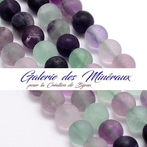 Peut inclure: Un brin de perles rondes translucides dans des tons de vert, violet et noir. Les perles sont en fluorite et mesurent environ 8 mm de diamètre. Les perles sont enfilées sur un cordon élastique transparent. L'image comprend le texte "Galerie des Minéraux pour la Création de Bijoux".