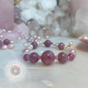 May include: A beaded bracelet featuring large, round, pink gemstones interspersed with smaller pink beads and white pearls. The bracelet is set against a soft, blurred background of other gemstones and pearls, creating a serene and elegant aesthetic.
