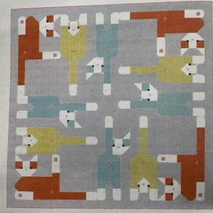 Op de afbeelding: Vierkante grijze stof met een herhalend patroon van gestileerde katten in oranje, geel en blauw. De katten hebben witte accenten en zijn in een symmetrisch ontwerp gerangschikt. De stof heeft een grijze rand.