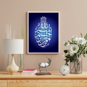 May include: A rectangular wall art print featuring white Arabic calligraphy centered on a deep blue background with a radial gradient, enclosed in a light-colored wooden frame. The artwork displays intricate script arranged in an oval shape.