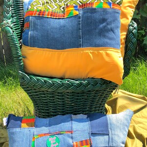 Pode incluir: Duas almofadas decorativas com patchwork de ganga e detalhes de tecido colorido. Uma almofada est&aacute; numa cadeira de vime verde e a outra numa superf&iacute;cie verde. As almofadas t&ecirc;m uma base de ganga com detalhes laranja e estampados.