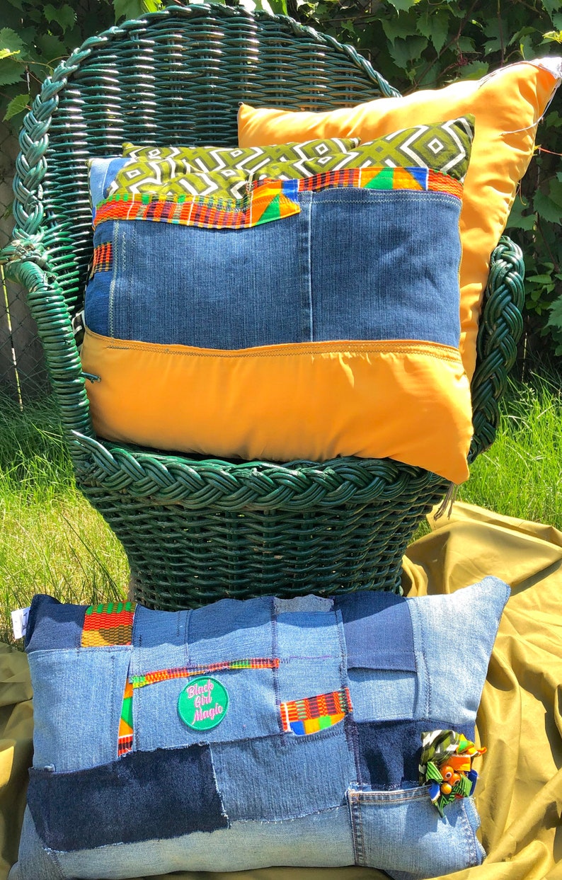 Pode incluir: Duas almofadas decorativas com patchwork de ganga e detalhes de tecido colorido. Uma almofada est&aacute; numa cadeira de vime verde e a outra numa superf&iacute;cie verde. As almofadas t&ecirc;m uma base de ganga com detalhes laranja e estampados.