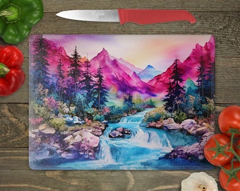 May include: A glass cutting board with a watercolor painting of a mountain scene with a waterfall. The mountains are pink, purple, and blue, and the waterfall is blue. There are trees in the foreground.
