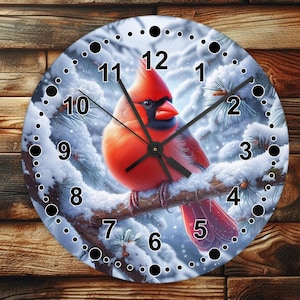 May include: A round clock with a white background and black numbers. A red cardinal bird is perched on a branch with snow-covered pine needles. The clock face has a wintery scene with snow and pine needles.