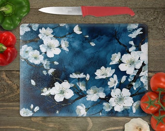 May include: A blue glass cutting board with a white floral design. The design features white cherry blossoms on branches against a blue background.