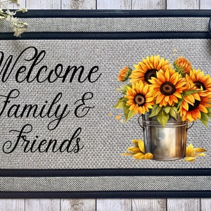 以下が含まれることがあります： グレーのジュート地の背景と黒い縁取りのあるウェルカムマット。マットの右側に、銀のバケツに入った黄色いひまわりの花束があります。マットには、「Welcome Family & Friends」という黒い筆記体で書かれた文字が印刷されています。
