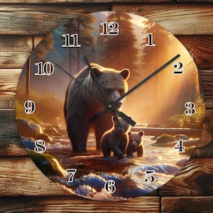 Puede incluir: Un reloj redondo con un oso marrón y dos cachorros en un entorno de bosque. La esfera del reloj tiene números romanos y manecillas negras. El fondo es una imagen borrosa de árboles y un arroyo.