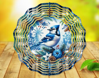 Könnte beinhalten: Ein blauer Vogel-Windspiel mit einem blauen und weißen Vogeldesign, umgeben von Kiefernästen, Beeren und Schneeflocken. Das Windspiel hat ein mehrschichtiges Design mit mehreren Kreisen.