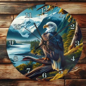 Könnte beinhalten: Runde Wanduhr mit einem majestätischen Weißkopfseeadler auf einem Ast. Das Zifferblatt zeigt schwarze Ziffern vor einer malerischen Kulisse aus Bergen, einem Fluss und blauem Himmel. Die Uhrzeiger sind schwarz.