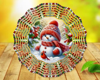 Könnte beinhalten: Dekorative Weihnachtskugel mit einem Schneemann, der einen roten Hut und Schal trägt, umgeben von Stechpalmen und Schnee. Die Kugel hat einen wellenförmigen, geschichteten Rand mit roten, grünen und goldenen Akzenten. Der Hintergrund ist verschwommen.
