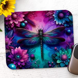 Puede incluir: Un ratón de ordenador con un diseño de libélula azul y morada con alas negras, rodeado de flores de colores. Las flores son de color rosa, morado y azul.