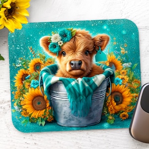 Può includere: Un tenero vitello Highland Cow con una corona di fiori turchese è seduto in un secchio di metallo circondato da girasoli su uno sfondo turchese.