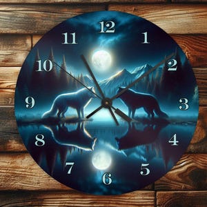 Op de afbeelding: Een ronde klok met een blauwe en zwarte achtergrond waarop twee wolven naar de maan huilen. De wijzerplaat van de klok heeft Romeinse cijfers en een zilveren wijzer. De klok is geplaatst tegen een houten achtergrond.