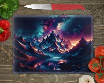 May include: Rectangular glass cutting board featuring a vibrant mountain landscape with a lake, under a colorful night sky. A stainless steel knife with a red handle rests above the board. Fresh vegetables surround the board.