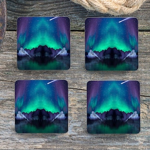 May include: Four square coasters featuring a colourful aurora borealis scene. The coasters depict a green and blue aurora borealis over a dark mountain range reflected in a still body of water. A single white shooting star streaks across the sky.