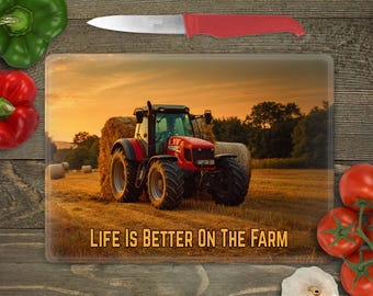 May include: Rectangular glass cutting board featuring a red tractor in a field with hay bales, under a sunset sky. The text "LIFE IS BETTER ON THE FARM" is displayed on the board. A red knife and fresh vegetables are also visible.