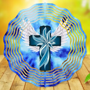 May include: A blue and white metal wind spinner with a cross and wings design. The cross is blue with a white flower design and white wings. The background is a blue and white watercolor pattern.
