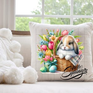 May include: A white cushion featuring a colourful illustration of a bunny rabbit sitting in a basket of spring flowers. The text "Hello Spring" is written in a decorative font below the bunny.