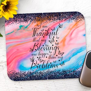 May include: A pink and blue marble-effect mouse pad with glitter accents and the text "I am thankful that my blessings are bigger than my problems" with butterfly illustrations.