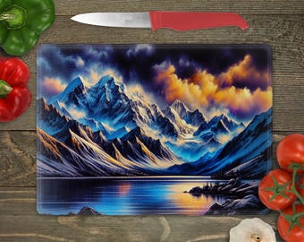 May include: A glass cutting board with a colorful mountain scene. The mountains are blue and white with a lake in the foreground. The sky is a vibrant orange and yellow with dark clouds.