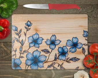 May include: A wooden cutting board with a floral design featuring blue flowers and leaves on a light wood background.