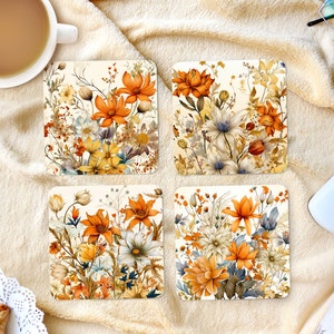 Puede incluir: Cuatro posavasos cuadrados con un diseño floral que presenta flores naranjas, amarillas y blancas sobre un fondo crema.