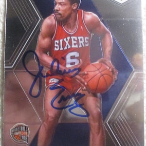 May include: A basketball trading card featuring Julius Erving in a red Sixers jersey with the number 6. The card has a mosaic design and includes the text "HALL OF FAME" and "PHILADELPHIA 76ERS". The card is autographed.