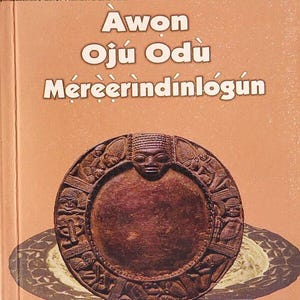 Puede incluir: Portada de libro con el título "Awon Oju Odu Mereerindinlogun" y el autor 'Wande Abimbola'. La portada presenta un relieve circular marrón con figuras humanas y una cara central, sobre un fondo melocotón.
