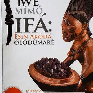 May include: Book cover with the title "ÌWÉ MIMO IFA" and the subtitle "ÈSIN AKÓDÁ ÓLÓDÙMARÈ". The cover features a wooden sculpture of a person holding a bowl of dark objects. The book has a red and white "Akotun 2023" sticker.