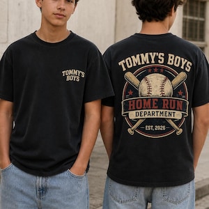 Op de afbeelding: Een zwart t-shirt met korte mouwen en een kleine afbeelding op de linkerborst met de tekst TOMMY'S BOYS. De achterkant toont een grote honkbalafbeelding met twee gekruiste knuppels, een honkbal en de tekst TOMMY'S BOYS HOME RUN DEPARTMENT EST, 2026.