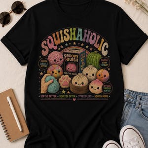May include: Black t-shirt with a colorful graphic featuring various squishy toys and the text "SQUISHAHOLIC." The design includes a rainbow arch, stars, and phrases like "Soft is Better" and "Squeeze Often."