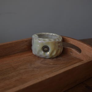 May include: A white ceramic planter with a textured surface and a small logo in the center. The planter is sitting on a wooden tray with a dark brown finish.