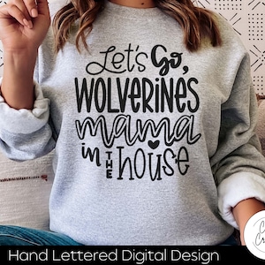 May include: Gray sweatshirt with the text "Let's Go, Wolverines mama in the house" in black lettering. The text is hand-lettered and includes a small heart.