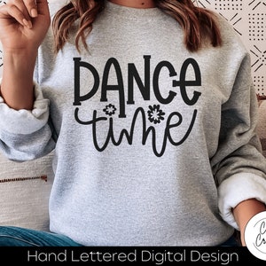May include: A gray sweatshirt with the text "Dance time" in black lettering. The text is hand-lettered and includes a small flower graphic.