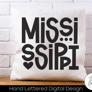 May include: White pillow with black text that reads "MISSISSIPPI" with a heart in the middle. The text is in a bold, hand-lettered style. The pillow is on a white brick background. The text "Hand Lettered Digital Design" is below the pillow.