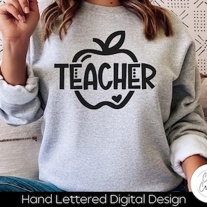 May include: A gray sweatshirt with a black apple graphic and the word "TEACHER" inside the apple. The sweatshirt is a hand-lettered digital design.